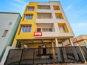 A multi-story building with a yellow facade, a sign for 'OYO ROOMS,' and a gated entrance.