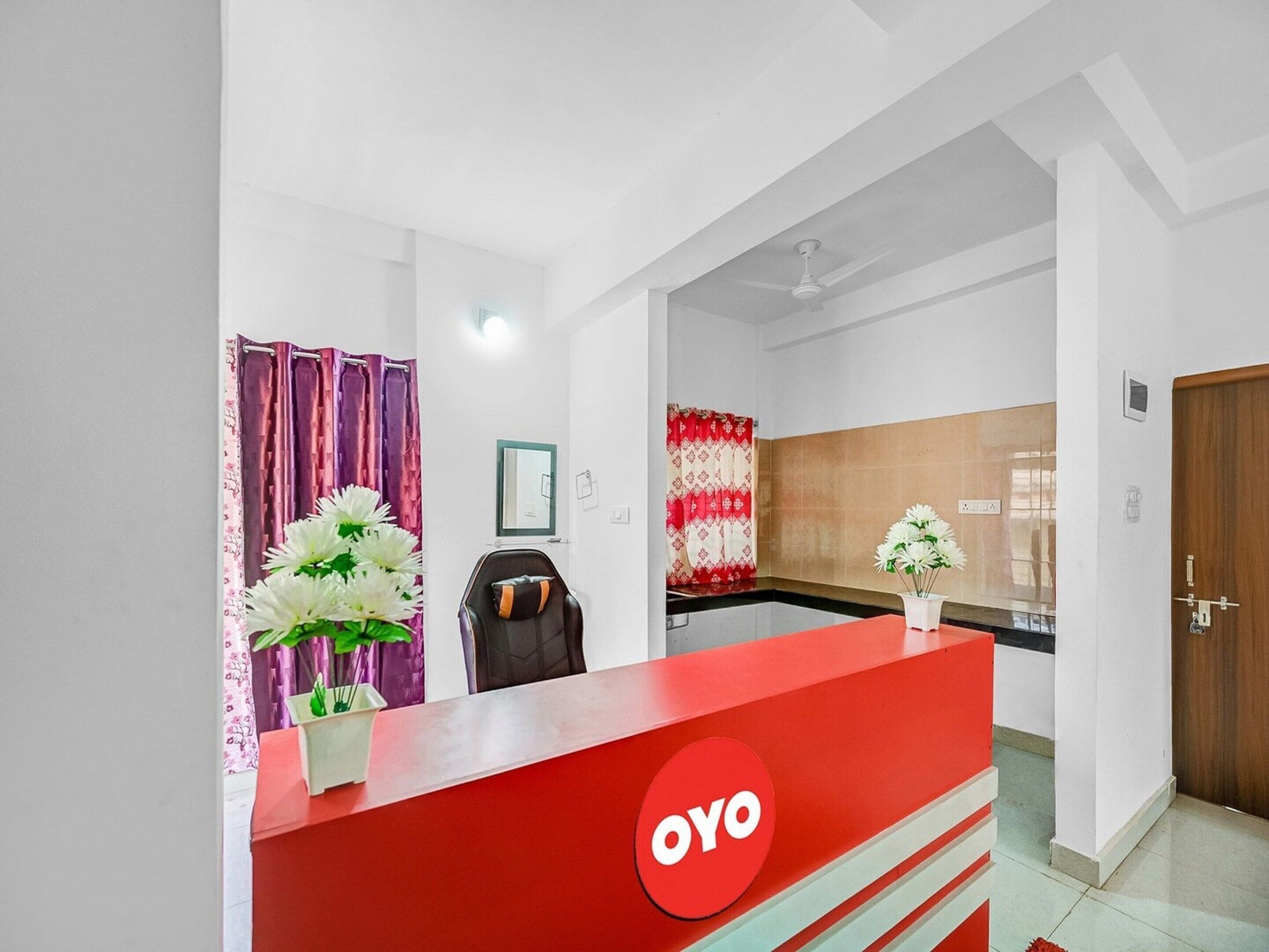 A reception area with a red counter, a chair, and a wall-mounted mirror.