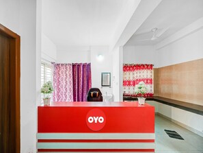 A reception area with a red counter, a white sink, and a chair. - Classic Dream Marion (Bhubaneshwar)
