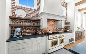 A kitchen with a brick wall, white cabinetry, a gas stove, and a mixer. - Private 30A Resort: Infinity Pool, Gym, Pickleball, 2 min. to Beach. Must see! (Santa Rosa Beach)