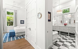 Et moderne soveværelse med en seng, en blå bænk, en hvid dør og udsigt til et badeværelse med skakmønstret gulv.