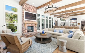 A spacious living room with a brick fireplace, a large sofa set, and a dining area with wicker furniture. - Private 30A Resort: Infinity Pool, Gym, Pickleball, 2 min. to Beach. Must see! (Santa Rosa Beach)