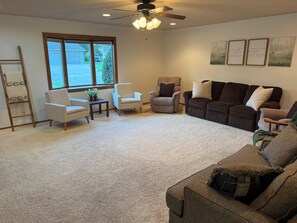 A living room with a ceiling fan, a large window, and a dark brown sofa with multiple pillows.