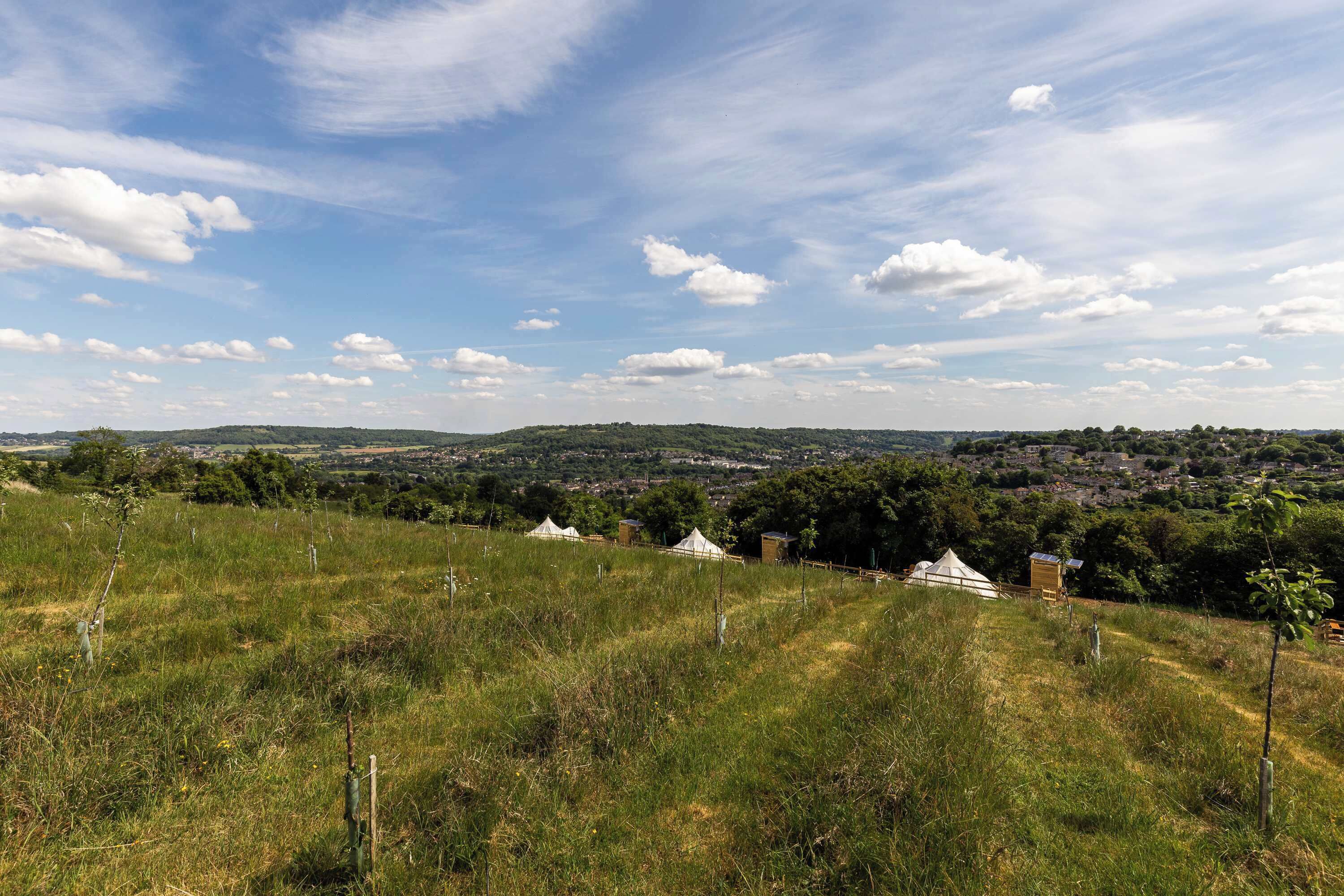 Une colline verdoyante d’où l’on aperçoit une ville au loin, un ciel dégagé et quelques tentes.