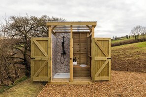 A wooden outdoor shower structure with a stone wall, a sink, and a toilet.