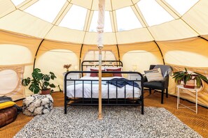 A cozy tented room with a bed, a chair, and a small table with a plant.