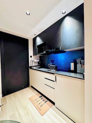 A modern kitchen with a black door, a stainless steel range hood, and a wooden floor. - Altura View Palace Apartment (Nairobi)