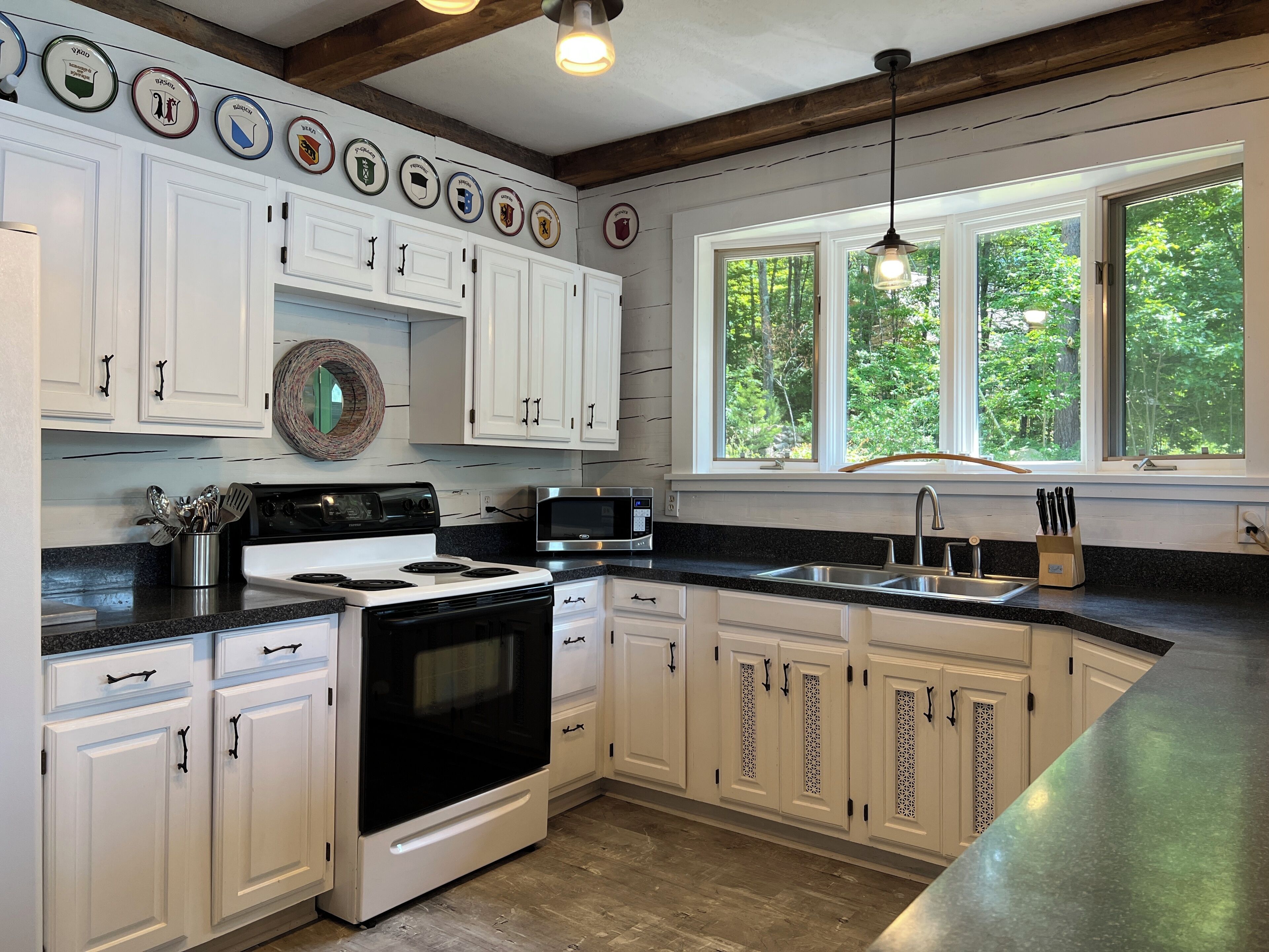 A kitchen with white cabinets, a black stove, a microwave, and a window with a view of trees.