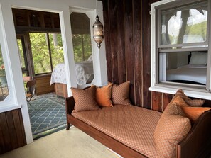 Een houten bed met gestreepte kussens, een raam met uitzicht op groen, en een decoratieve lantaarn.