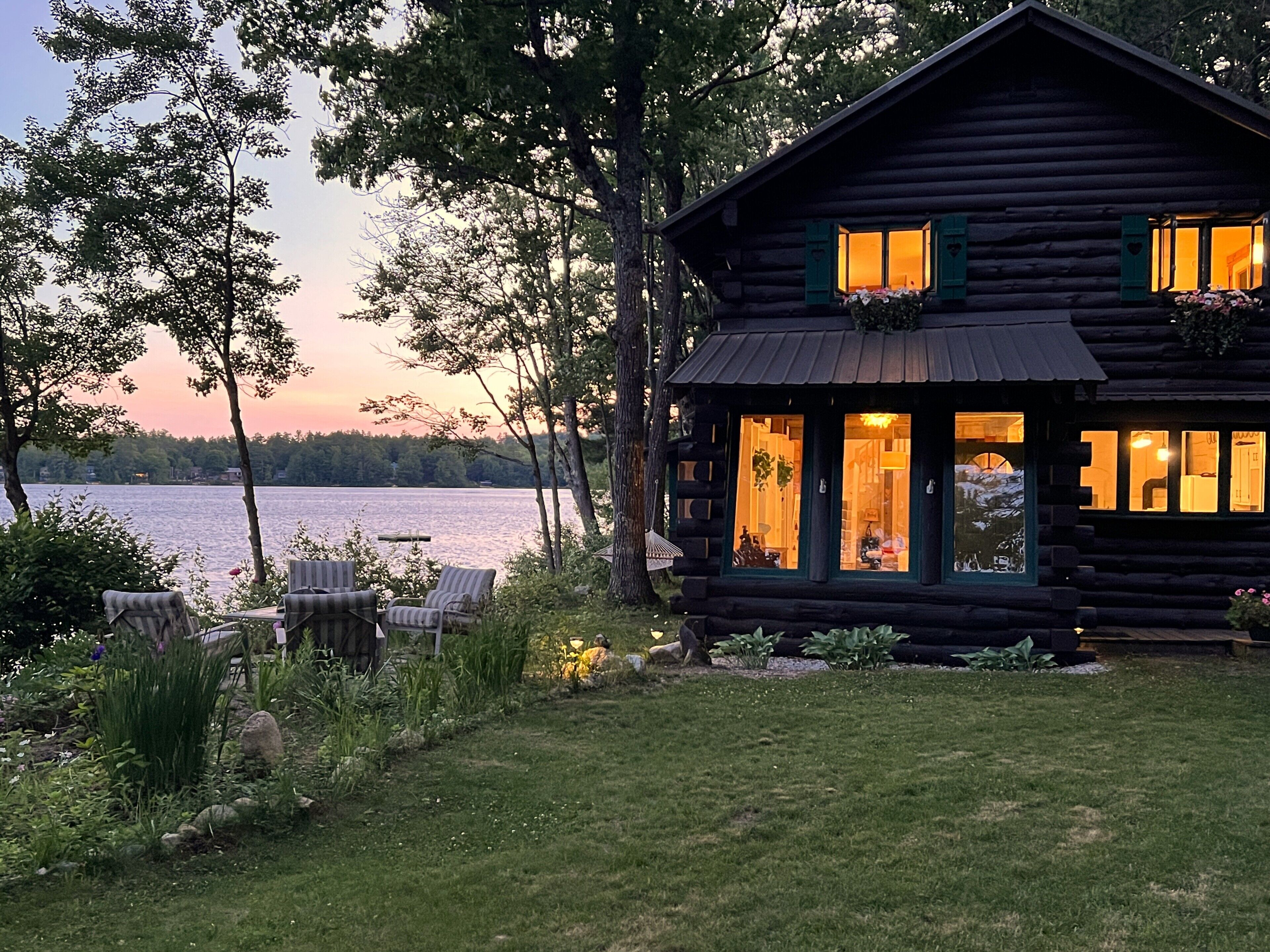 A log cabin with a view of a lake, outdoor seating, and a well-maintained garden.