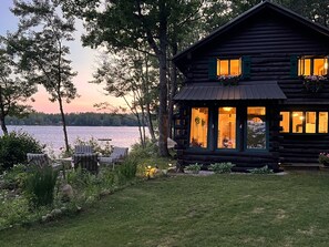 Eine Blockhütte mit Seeblick, Sitzgelegenheiten im Freien und einem gepflegten Garten.