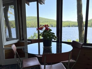 Ein Zimmer mit einem runden Tisch, Stühlen, einer Topfpflanze und Blick auf einen See und Wald.