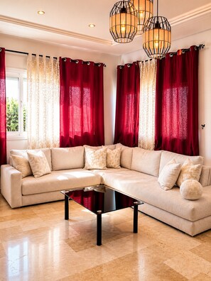 Ein modernes Wohnzimmer mit einem beigefarbenen Ecksofa, einem Glastisch und roten Vorhängen.
