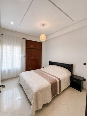 A bedroom with a bed, a nightstand, a wardrobe, and a ceiling light fixture. - Family Apartment for 4–5 People (Fes)