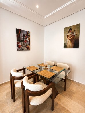 A dining area with a glass table, woven placemats, and cushioned chairs. - Family Apartment for 4–5 People (Fes)