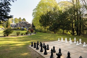 Un grand jeu d’échecs en plein air, installé sur une pelouse, avec un bâtiment en arrière-plan.