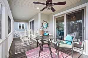 Eine überdachte Veranda mit Deckenventilator, Schaukelstühlen, einem Tisch mit Stühlen und einem Teppich.