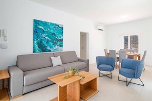 A modern living room with a grey sofa, blue armchairs, a wooden coffee table, and a large abstract painting on the wall. - Villa Verde Yaiza by Villa Plus (Playa Blanca)