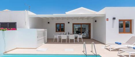 A pool area with a table and chairs, a covered seating area, and a clear blue sky.