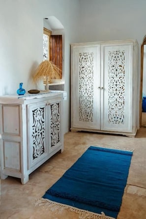 A room with a white cabinet with intricate carvings, a blue rug, and a white door with detailed patterns.