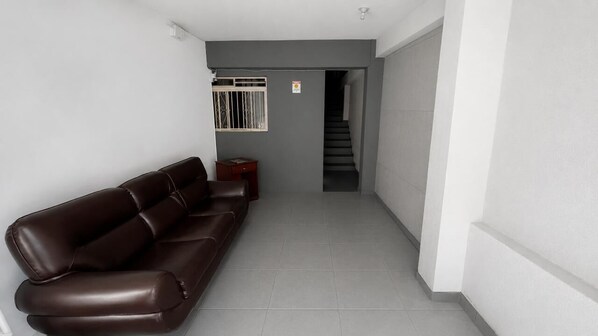 A hallway with a brown leather sofa, a small wooden table, and a staircase leading to another floor. - Aconchego de Lugar - Eri & Douglas - 2 (Belo Horizonte)