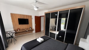 Una habitación de hotel moderna con una cama grande, un televisor de pantalla plana montado en un panel de madera, un escritorio pequeño con una silla y una puerta corredera para el armario.