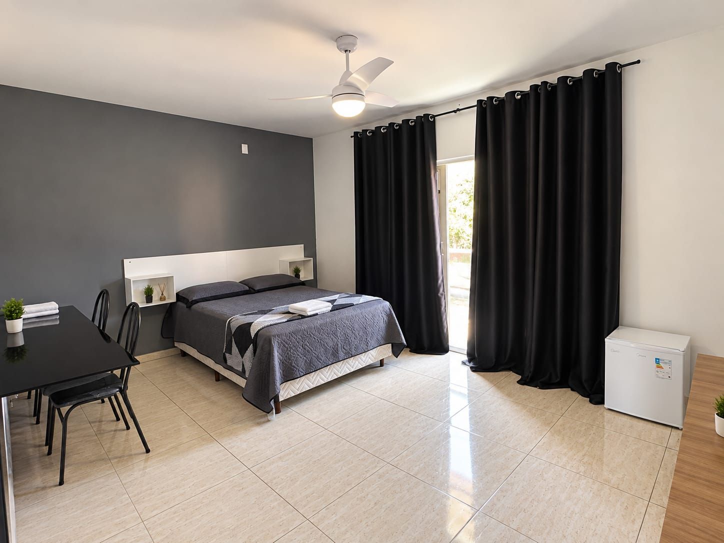 Un dormitorio moderno con cama, escritorio y un refrigerador pequeño.