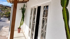 Un edificio con fachada blanca, una pérgola de madera y un cactus en maceta.