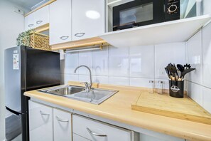 A modern kitchen with white cabinets, a black refrigerator, a stainless steel sink, and a wooden countertop. - Prime Apartment - MUT y Costanera Center (Las Condes)