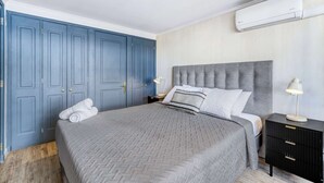 A bedroom with a bed, a nightstand, a lamp, a wardrobe, and an air conditioning unit. - Prime Apartment - MUT y Costanera Center (Las Condes)