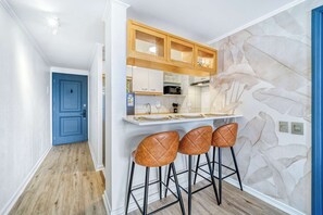 A modern kitchen with a stone accent wall, a blue door, and three leather bar stools. - Prime Apartment - MUT y Costanera Center (Las Condes)