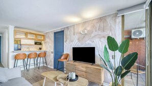 A modern living room with a sofa, a coffee table, a TV, and a dining area with bar stools. - Prime Apartment - MUT y Costanera Center (Las Condes)