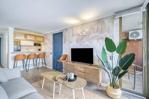 A modern living room with a sofa, a coffee table, a TV, and a dining area with bar stools. - Prime Apartment - MUT y Costanera Center (Las Condes)