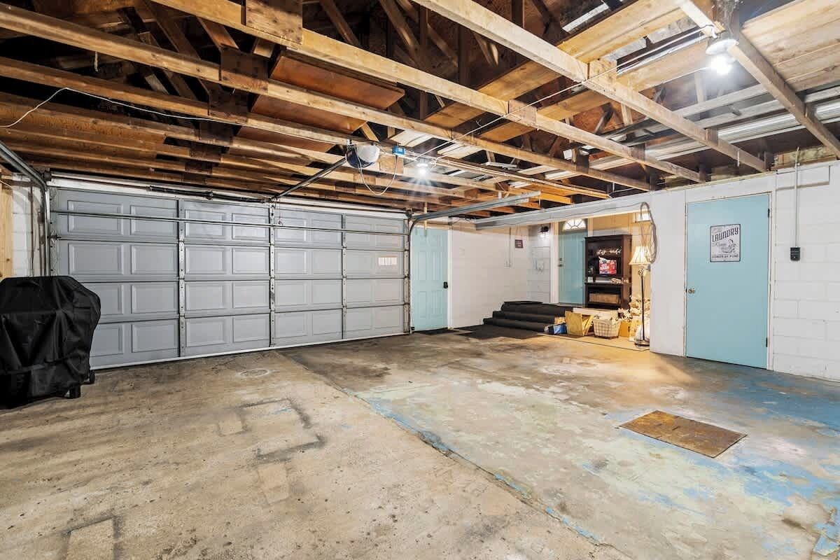 Un garage avec deux portes de garage blanches, un véhicule à l’abri et un petit espace boutique avec des marches menant à une porte.