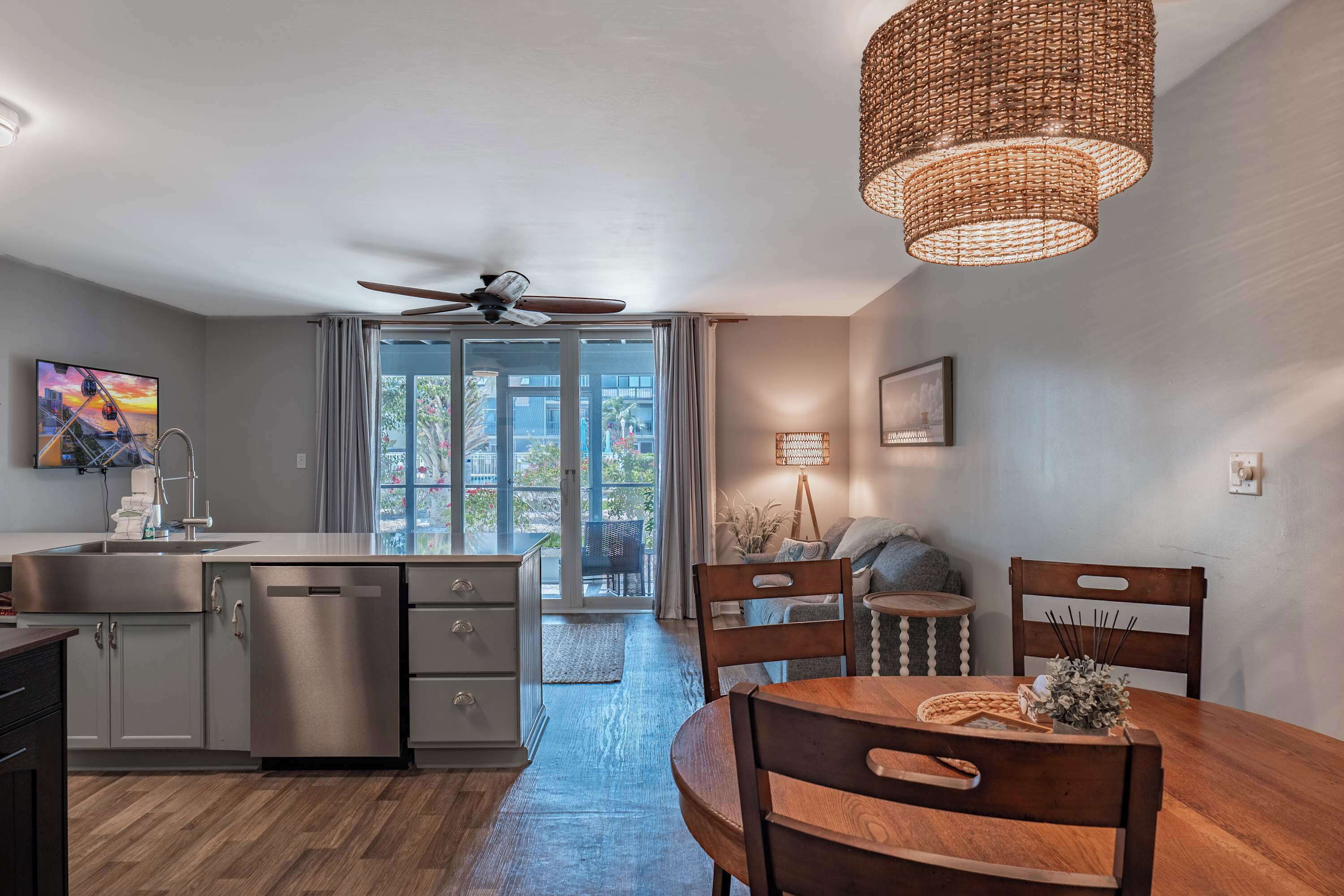 A modern kitchen with a dishwasher, a dining table with chairs, a ceiling fan, and a large window with curtains.