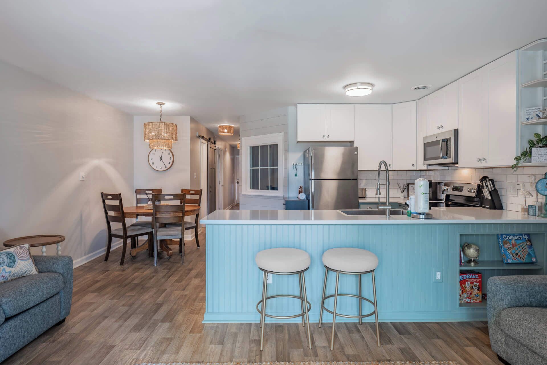 A modern kitchen with a central island, stainless steel appliances, and a dining area with wooden chairs and a blue sofa.