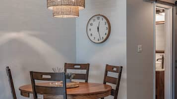 A dining area with a round wooden table, four chairs, a wall clock, and a hanging light fixture.