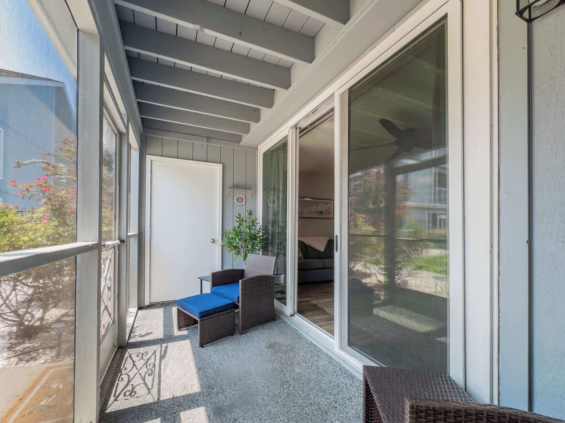 A covered balcony with a seating area, a sliding glass door, and a view of the outdoors.