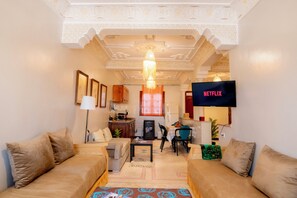 Ein Wohnzimmer mit einer Sofagarnitur, einem Fernseher und einer Küche im Hintergrund.