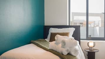 A hotel room with a bed, a window, and a bedside table with a lamp.