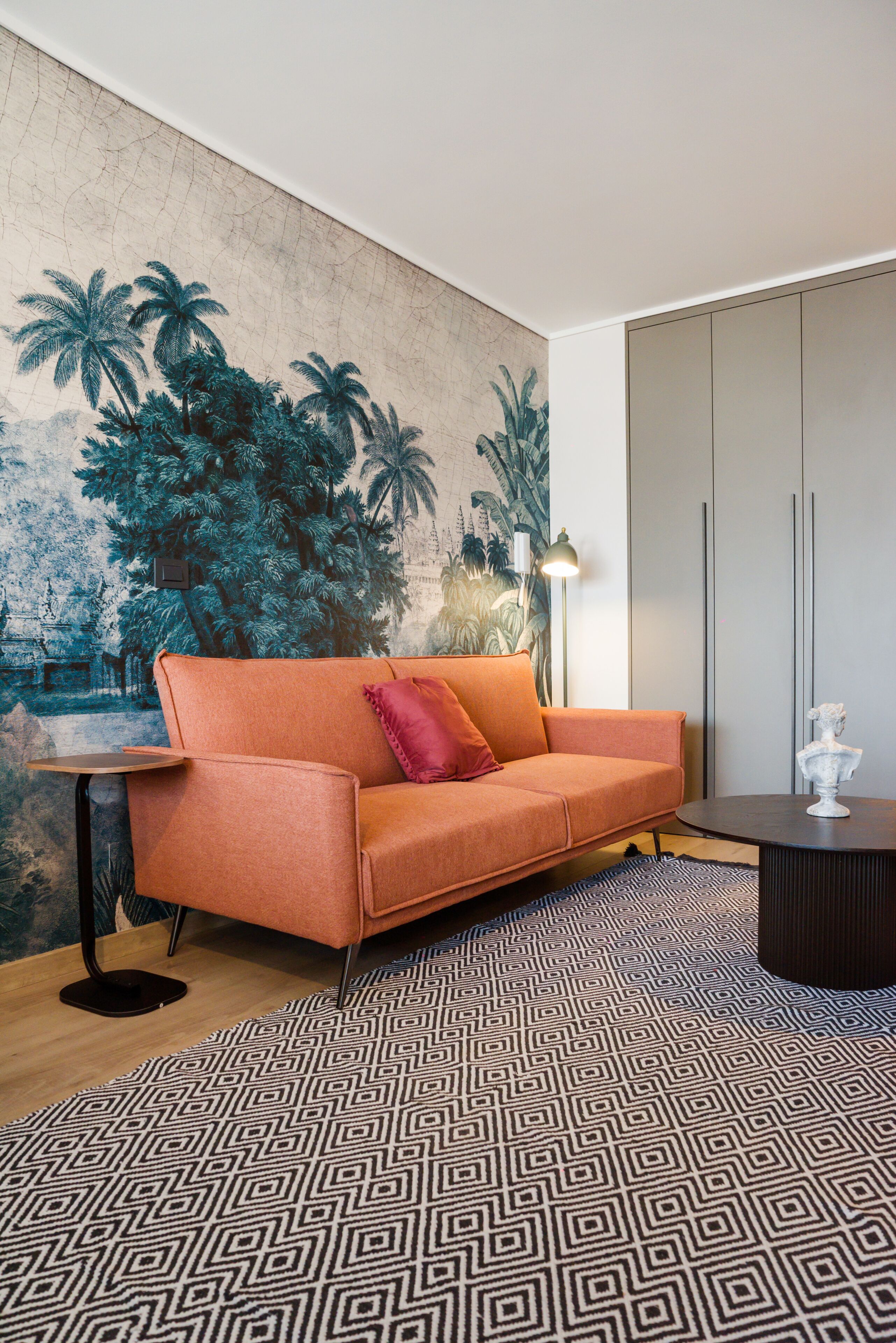 A modern living room with a sofa, a patterned rug, a lamp, and a wall mural.