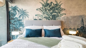 Un lit avec une tête de lit grise, deux oreillers, un plaid vert et du linge de lit blanc.