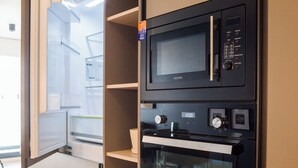 Une cuisine équipée d’un four à micro-ondes et d’un four encastrés, d’un meuble en bois et d’un réfrigérateur à porte en verre.