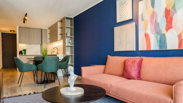 Un salon moderne avec un canapé, des fauteuils, une table basse et une cuisine en arrière-plan.