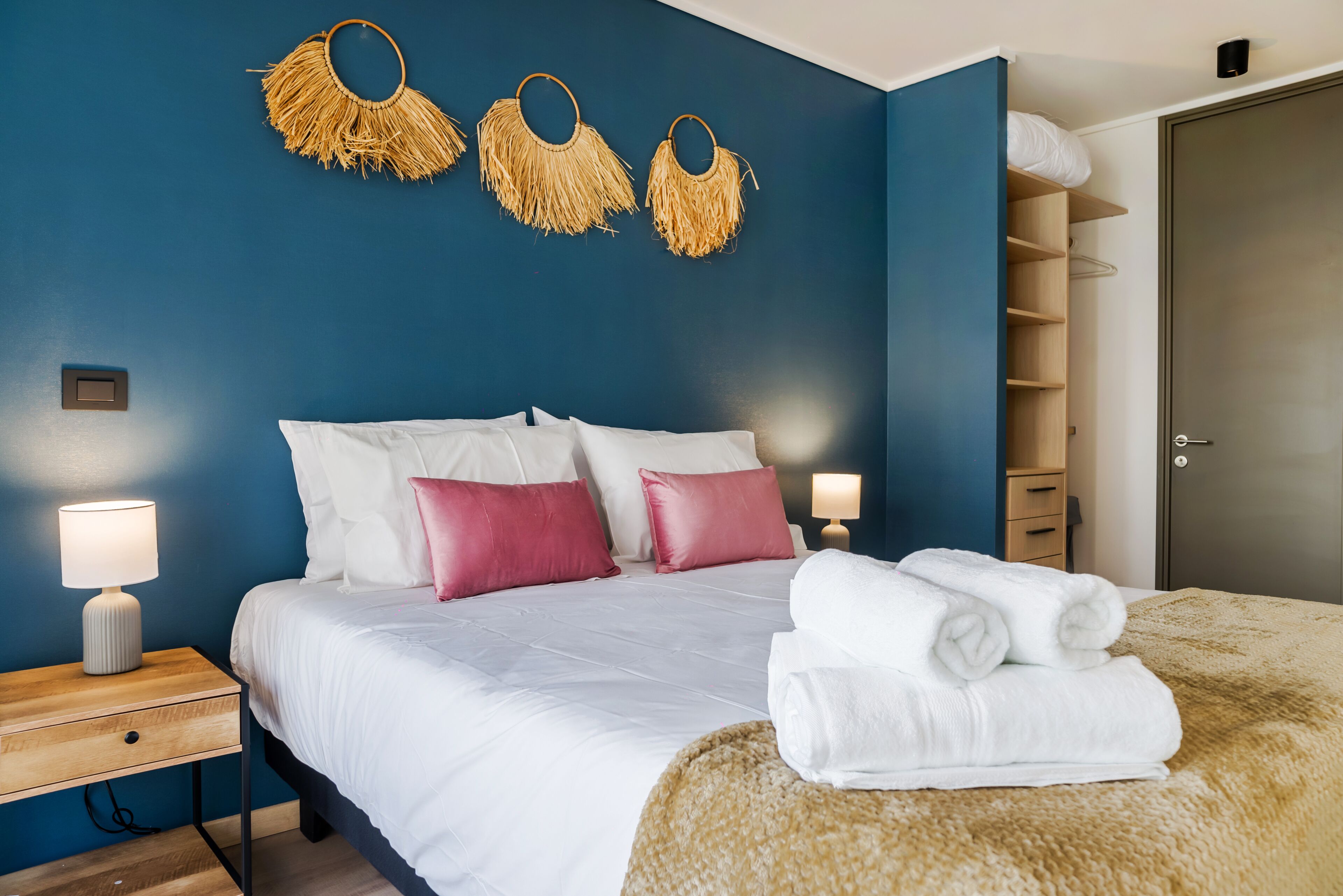 A hotel room with a bed, pillows, a bedside table, a lamp, and a wardrobe.