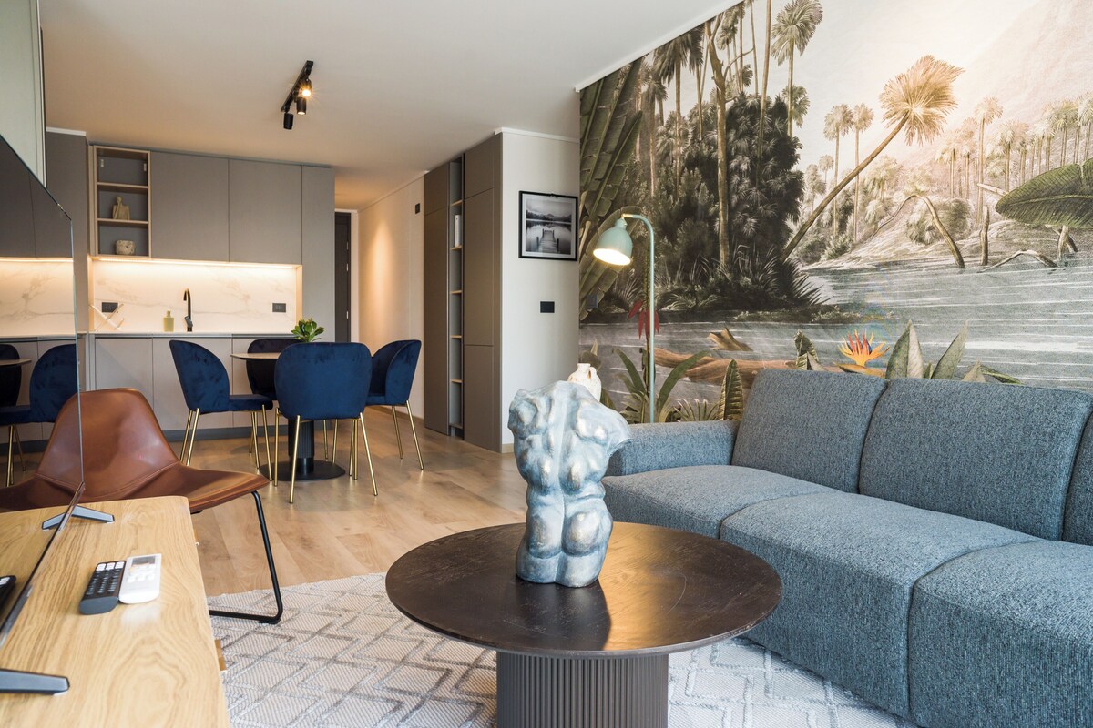 Una sala de estar moderna con un sofá gris, una mesa de centro redonda y una zona de comedor con sillas azules.