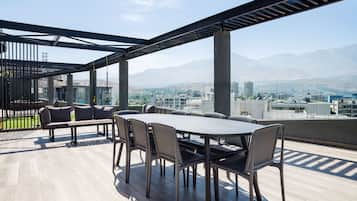 An outdoor terrace with a dining table and chairs, overlooking a cityscape and mountains.