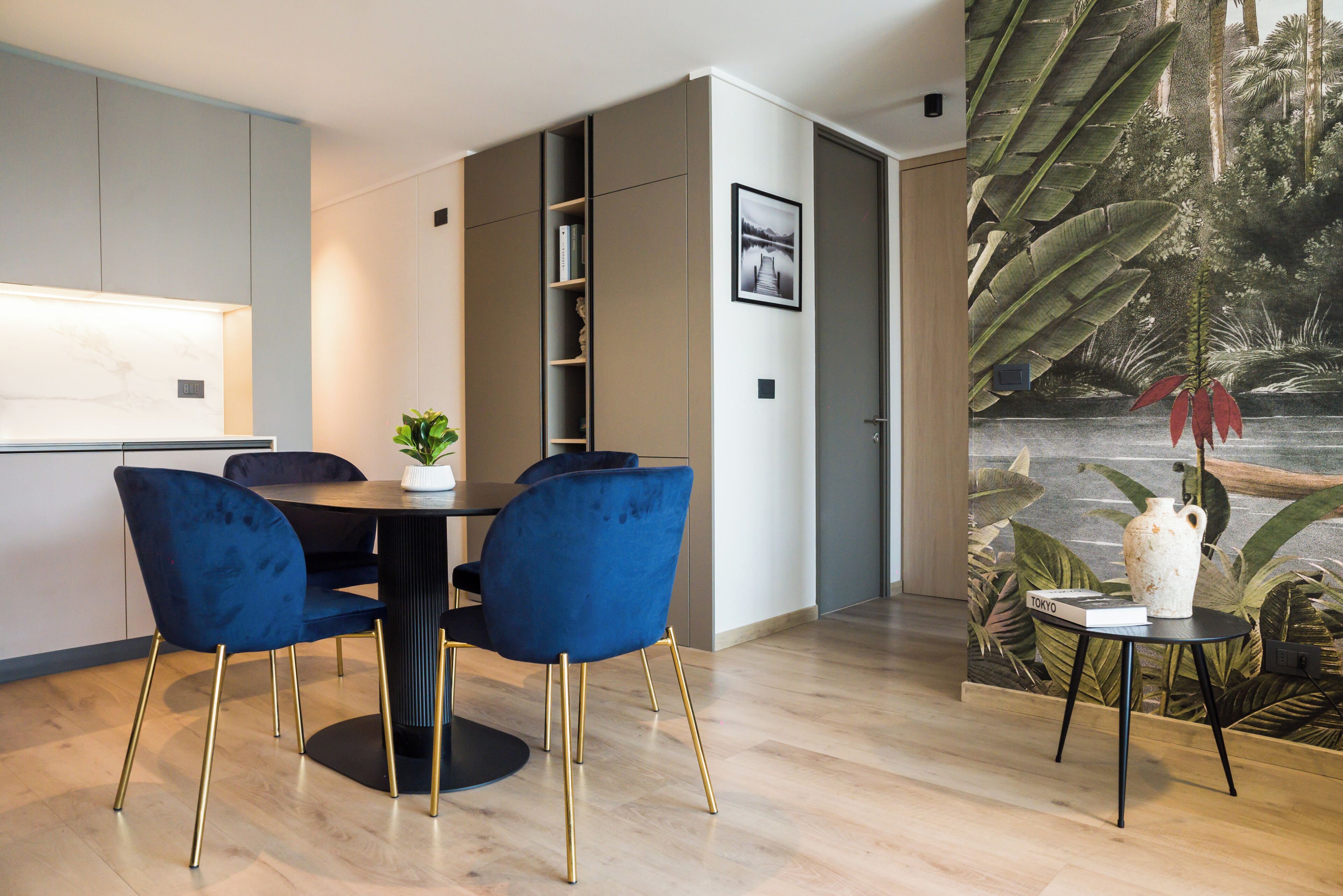 A modern dining area with a round table, two blue chairs, and a small side table with a vase.