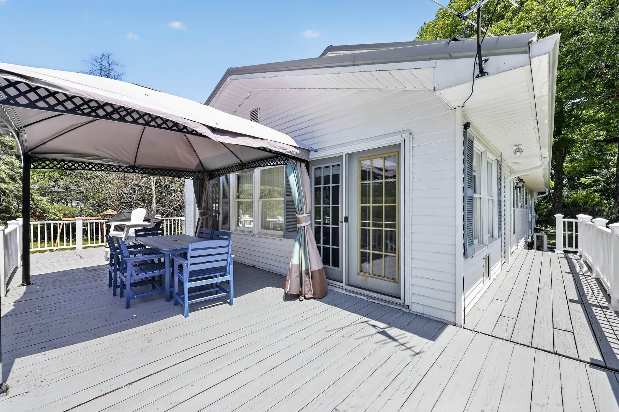 A covered outdoor deck with a table and chairs, a pergola, and a house with large windows.