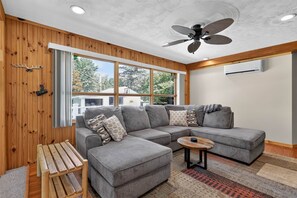 Ein modernes Wohnzimmer mit einer Eckcouch, einem Holztisch und einem Deckenventilator.